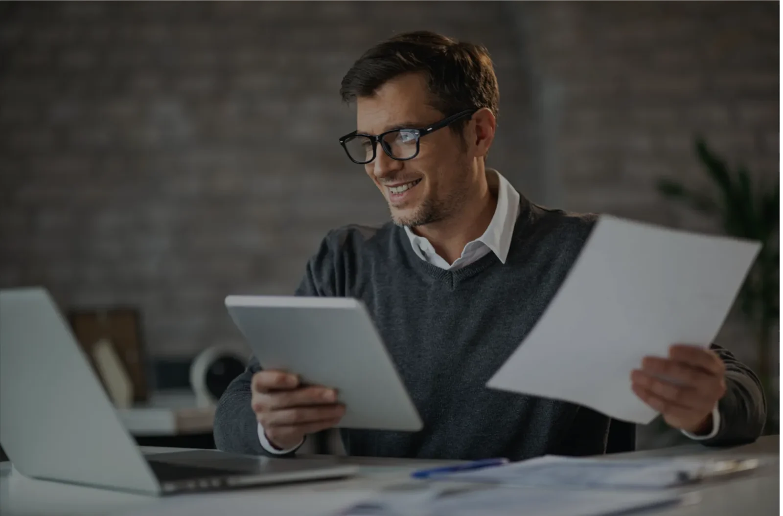 Business man in a sweater looking at papers at his desk and smiling