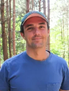 Man in a ball cap and blue t-shirt standing in the woods