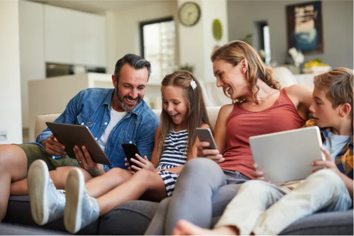 Family sitting on the couch using various electronic devices