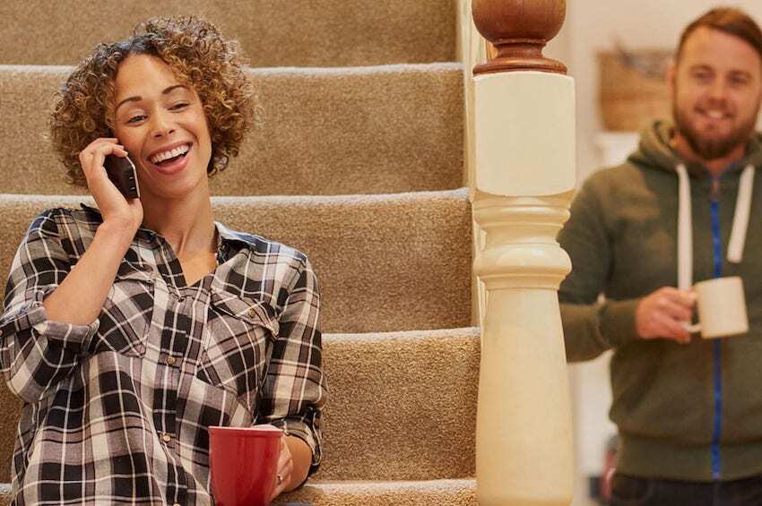 Woman sitting on staircase talking on the phone and drinking coffee while smiling man looks on