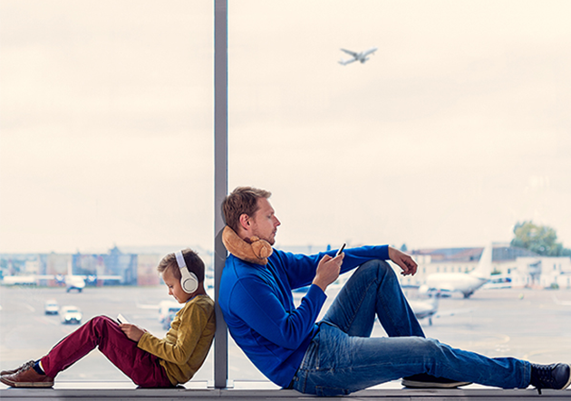 Father and son watching tv on phones at the airport