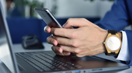 Hands holding phone over open laptop