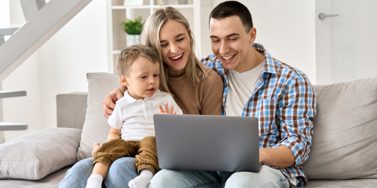 mom, dad, and child sit on couch with laptop on lap open.