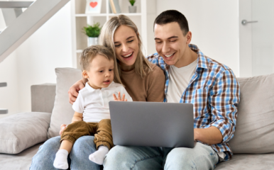 mom, dad, and child sit on couch with laptop on lap open.