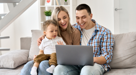 mom, dad, and child sit on couch with laptop on lap open.