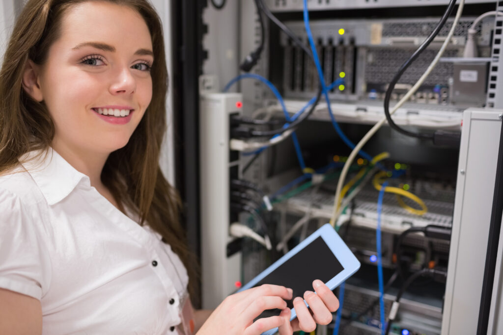 A smiling woman standing in front of a data center rack filled with networking equipment, holding a tablet and monitoring connections. Who is my service provider?"