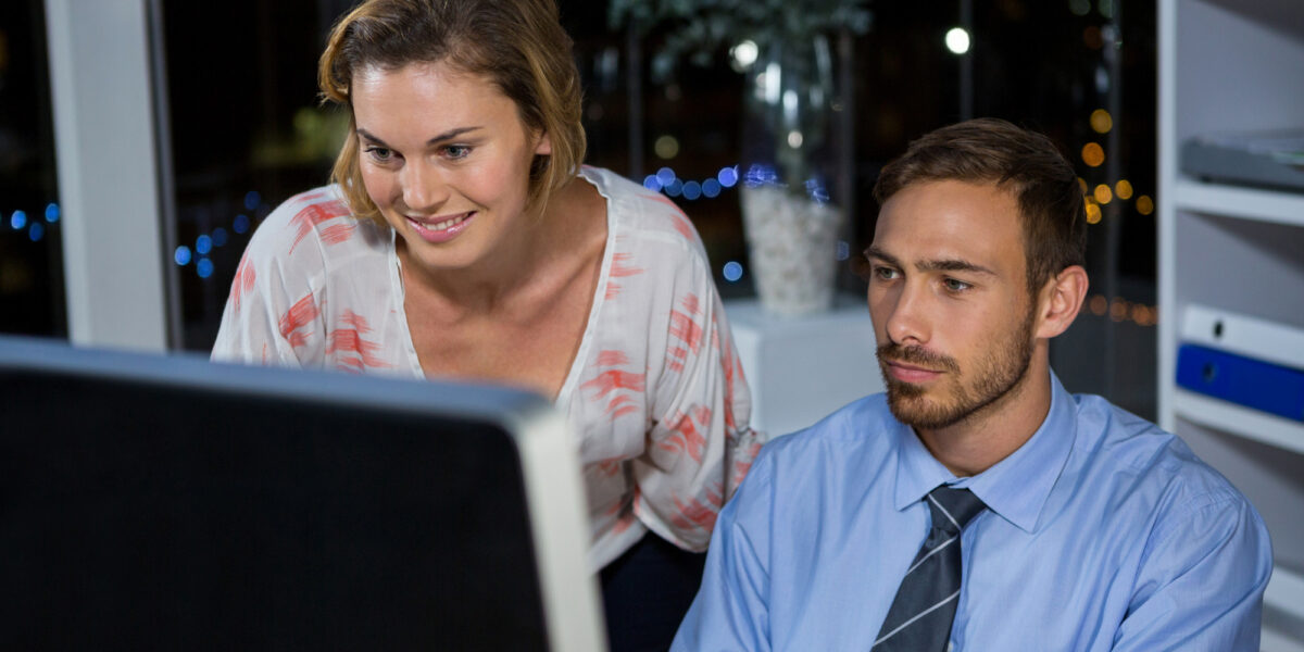 Two business executives collaborate on a computer in a modern office, emphasizing the role of business fiber optic internet in ensuring efficient teamwork and smooth operations.