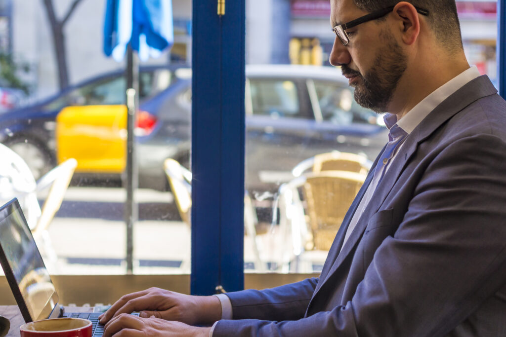 A professional in a suit works on his laptop near a café window, showcasing the power and reliability of business fiber optic internet for remote work and productivity.