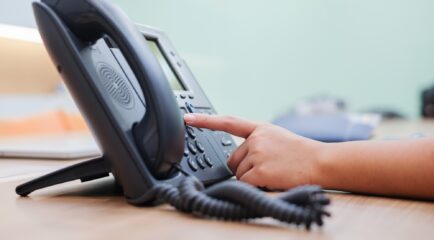 A close-up of a person’s hand dialing a number on a landline phone at an office desk, showcasing the importance of the best landline phone service for seamless and consistent connectivity in professional settings.