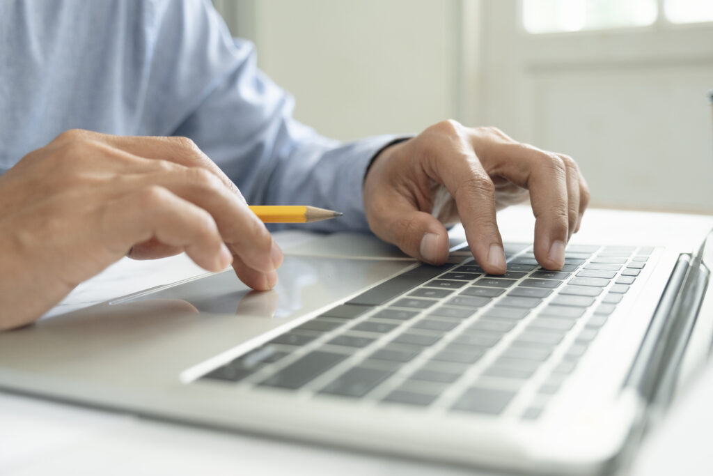 Close-up of a person typing on a laptop keyboard with a pencil in hand, symbolizing multitasking and a need to "check my computer speed" for efficient performance.