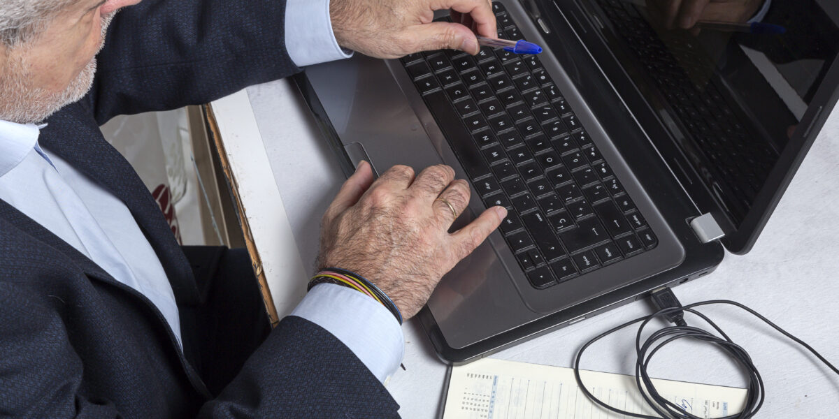 Mature man in a suit working on a laptop with a pen in hand, reflecting a professional setting where "check my computer speed" ensures optimal workflow and responsiveness.