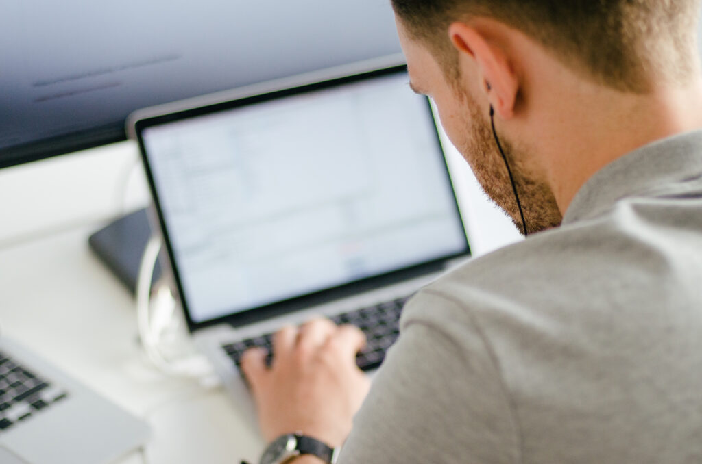 Rear view of a man working on a laptop, focusing on coding or technical work, highlighting the importance of knowing how to "check my computer speed" for seamless productivity.