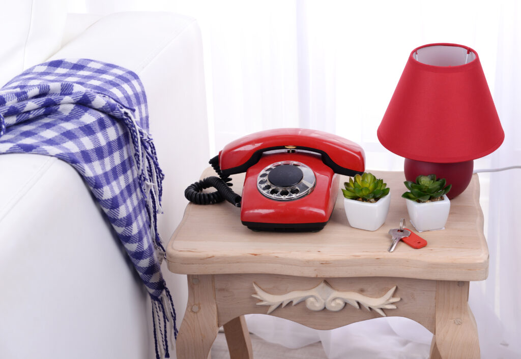 A vintage red rotary phone on a wooden nightstand next to small potted plants and a lamp, symbolizing a nostalgic approach to "home phone connect."