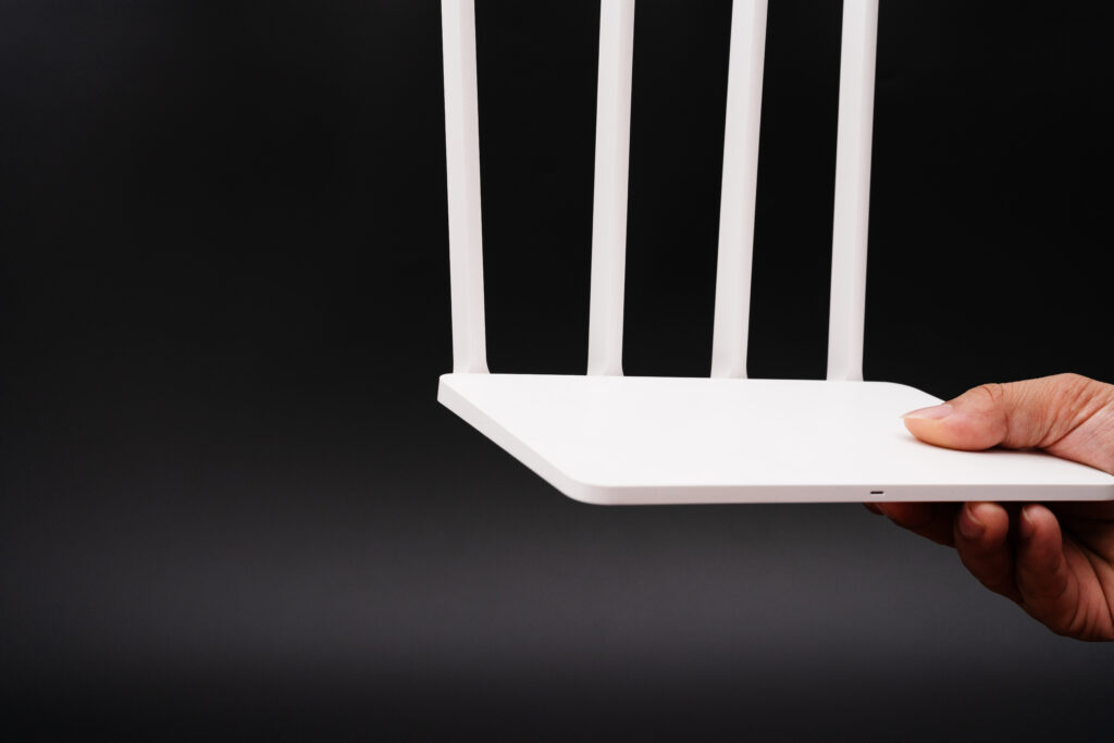 A sleek white router with four antennas held against a black background by a hand, emphasizing its modern design and advanced features. "When considering how often you should replace your router, ensure you choose models that meet your current connectivity needs."