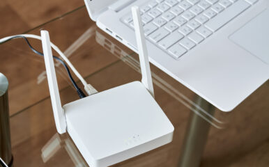 A close-up of a white internet box for home with antennas and ethernet cables connected, sitting next to a laptop on a glass desk for high-speed internet access.
